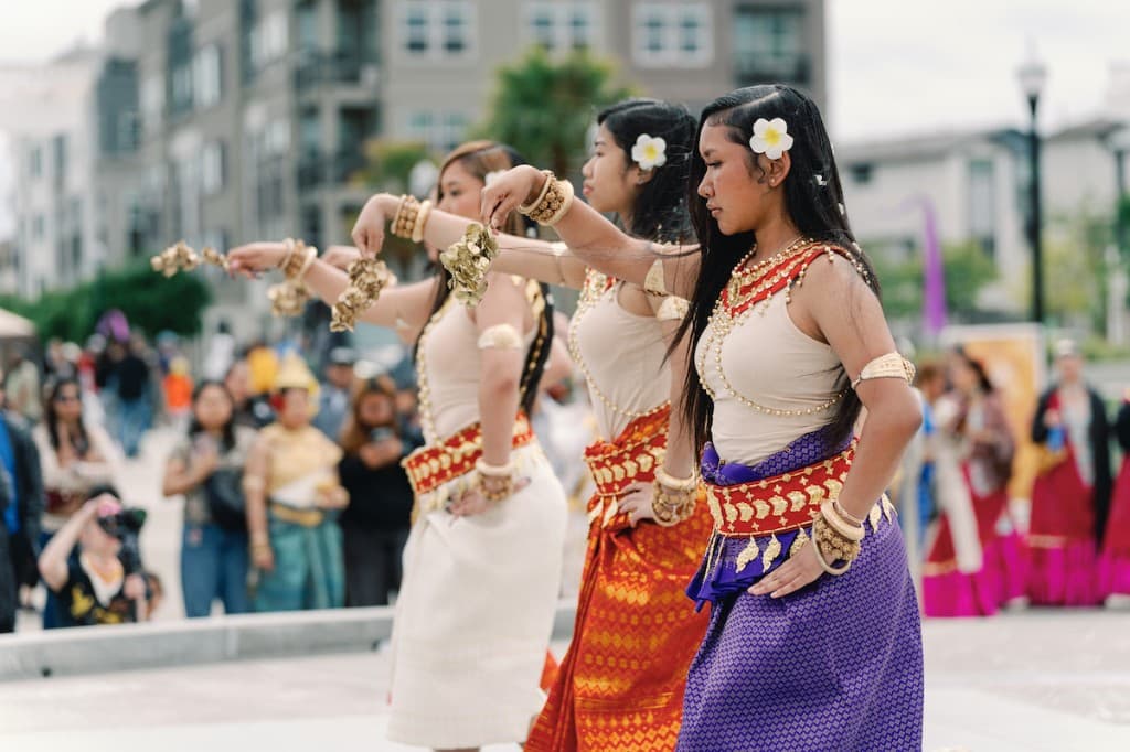 Traditional Cambodian dancers in silk costumes and gold jewelry performing outdoors for a community audience