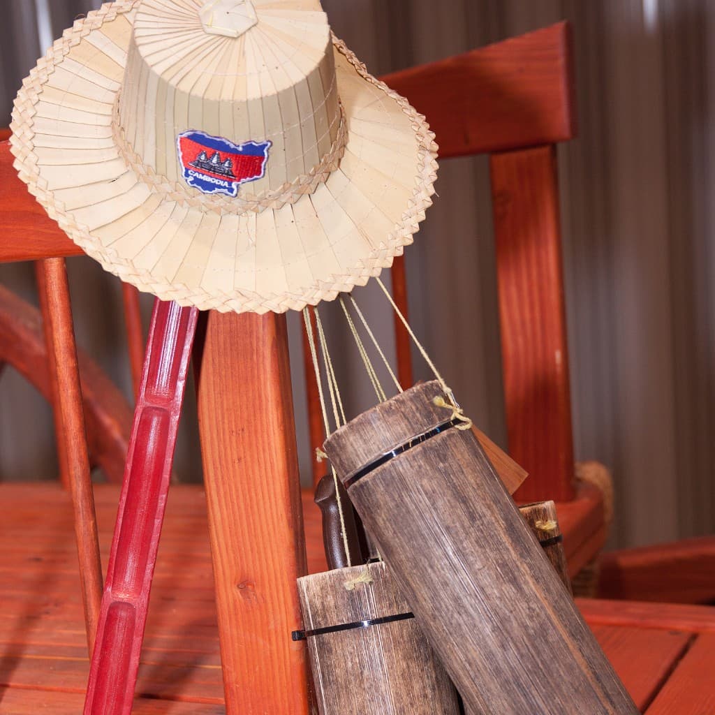 Traditional woven hat with a Cambodia flag patch, beside wooden and bamboo cultural items